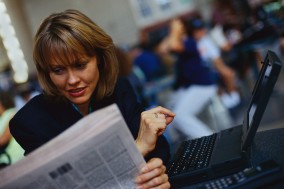 Businesswoman With Laptop Reading Newspaper